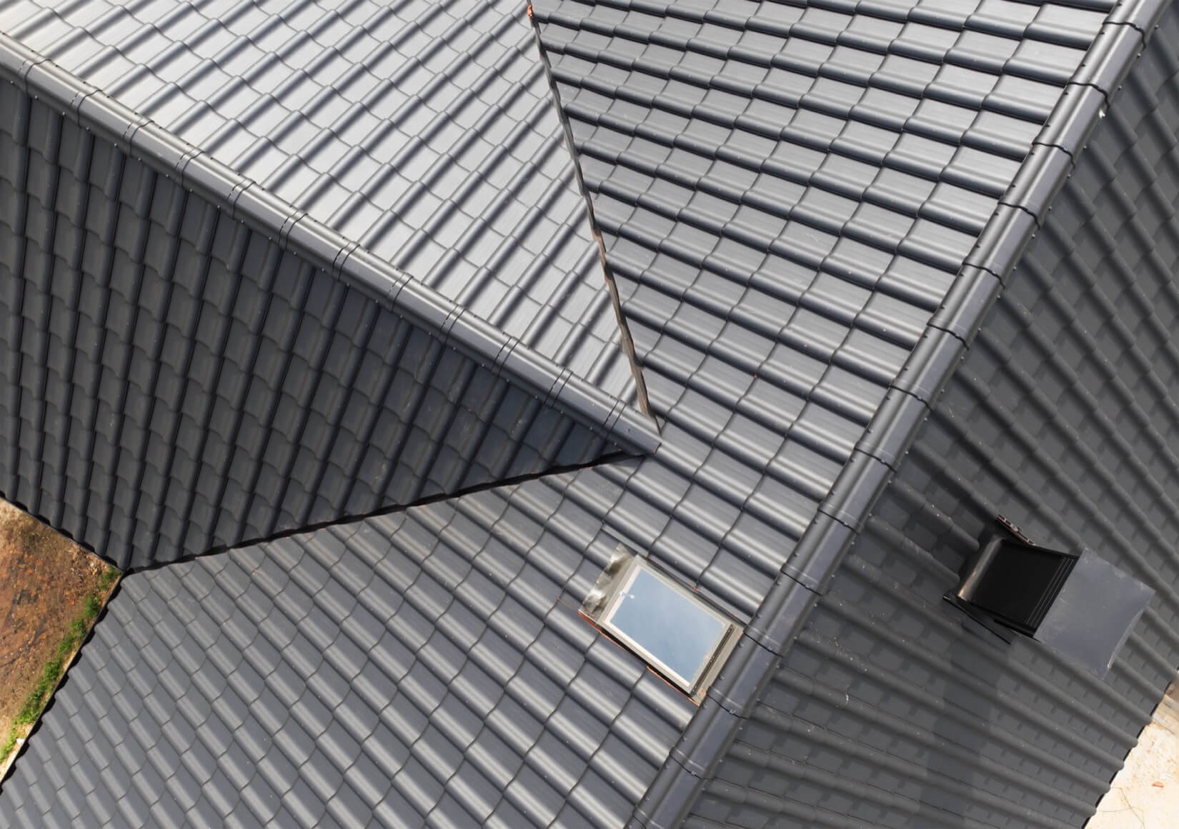 Ilmakuva, jossa näkyy monimutkainen katto, jossa on tummia betonilaattoja, kattoikkunoita ja kulmia, ja joka havainnollistaa edistyksellisen kattorakentamisen tulosta.